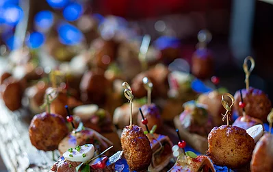 Bunte Spieße stecken in einer Auswahl an Häppchen und Fingerfood-Varianten, die auf einer rustikalen Holzplatte angerichtet sind